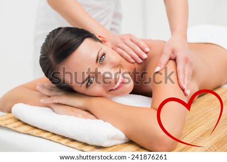 Beautiful brunette enjoying a shoulder massage smiling at camera against heart