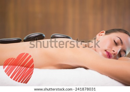 Beautiful woman receiving stone massage at health farm against red heart