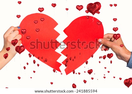 Two hands holding broken heart against red heart balloons floating
