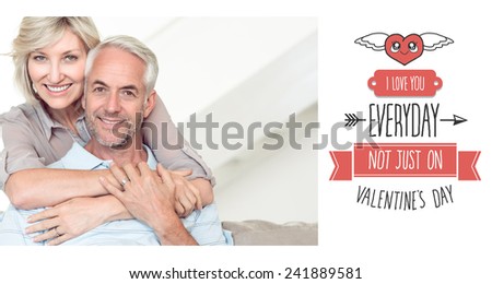 Smiling woman embracing mature man from behind on sofa against cute valentines message