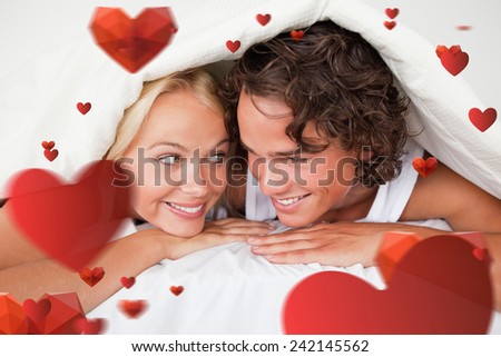 Couple under a duvet with a knowing smile against love heart pattern