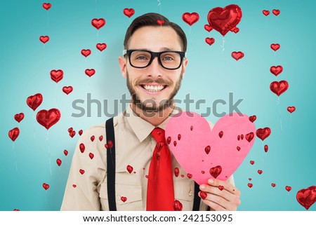 Geeky hipster smiling and holding heart card against blue vignette background