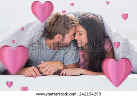 Cheerful couple head against head under the duvet against hearts