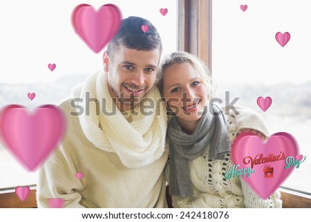 Couple in winter clothing sitting against window against cute valentines message