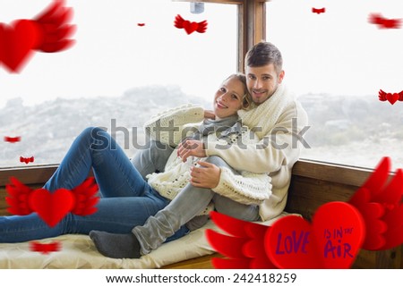 Couple in winter clothing sitting against cabin window against love is in the air