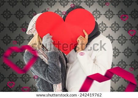Couple in winter fashion posing with heart shape against grey wallpaper