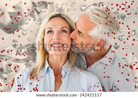 Affectionate man kissing his wife on the cheek against grey valentines heart pattern