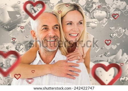 Happy man giving his partner a piggy back against grey valentines heart pattern