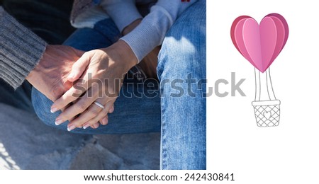 Couple holding hands sitting on sand against heart hot air balloon