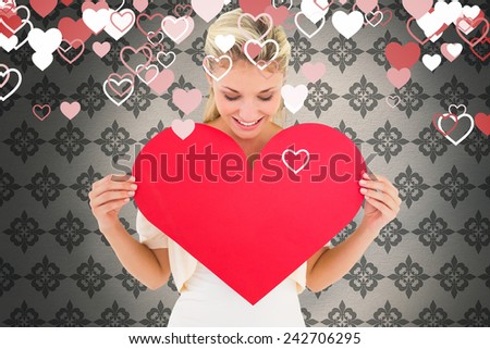 Attractive young blonde showing red heart against grey wallpaper