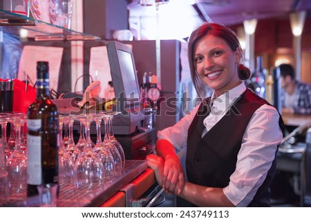 Happy barmaid using touchscreen till in a bar