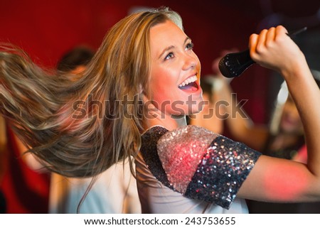 Happy blonde singing karaoke into mic in a bar