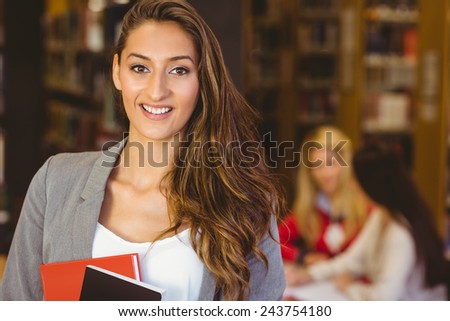 Portrait of a pretty brunette student holding books in library