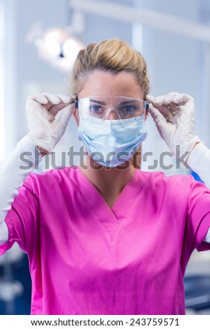 Dentist in pink scrubs looking at camera in mask and gloves at the dental clinic