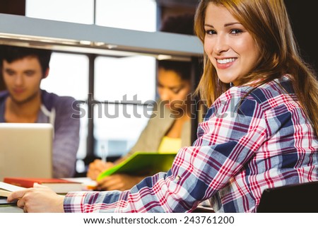 Portrait of a smiling student sitting at desk looking at camera in library
