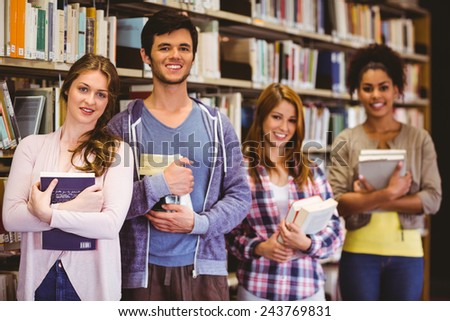 Happy students holding books in row in library