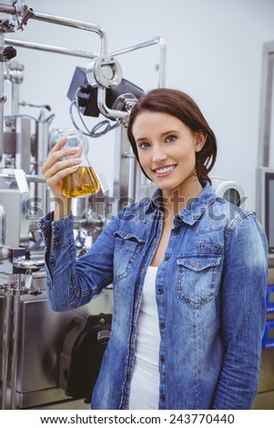 Smiling woman holding a beaker of beer in the factory