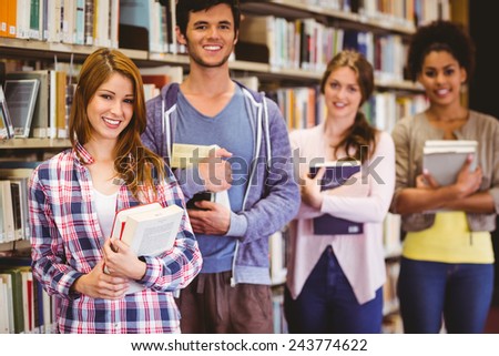 Happy students holding books in row in library