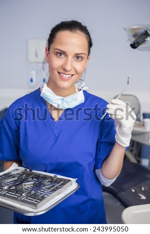 Smiling dentist holding tray and angle mirror in dental clinic