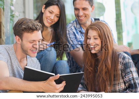 Happy students looking at book outside on campus at the university