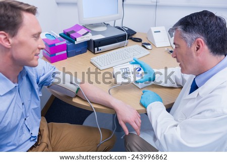 Smiling doctor measuring the blood pressure of his patient at the hospital