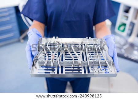 Dentist in blue scrubs holding tray of tools at the dental clinic