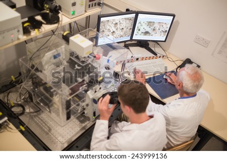 Biochemist and student looking at microscopic images on computer at the university