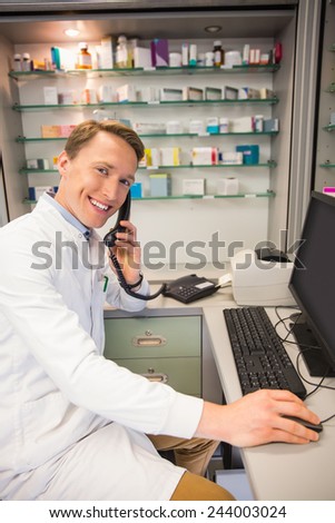 Happy pharmacist on the phone using computer at the hospital pharmacy