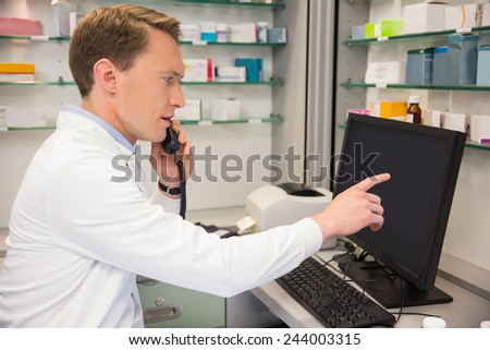 Serious pharmacist on the phone using computer at the hospital pharmacy