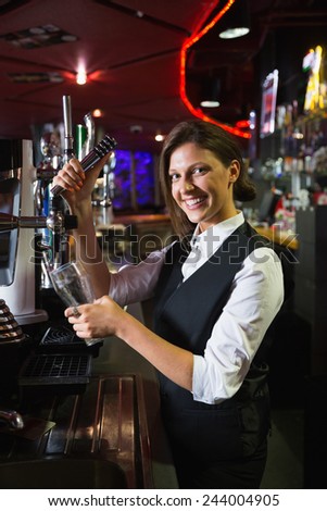 Happy barmaid pulling a pint of beer in a bar