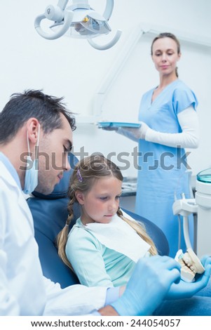 Male dentist teaching girl how to brush teeth in the dentists chair