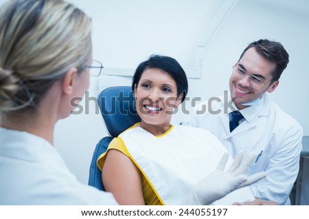 Portrait of smiling male dentist and assistant with female patient in the dentists chair