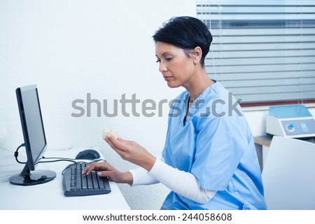 Concentrated female dentist looking at mouth model by computer