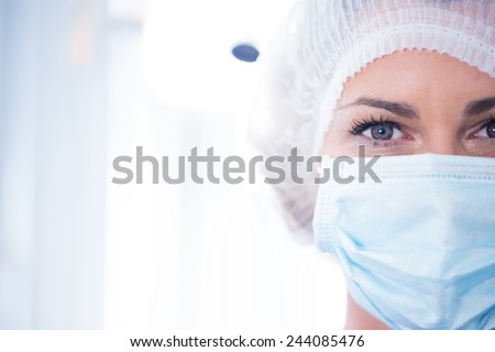 Dentist in surgical mask and cap looking at camera at the dental clinic