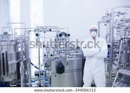 Scientist in protective suit standing with arms crossed in the factory