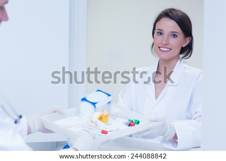Portrait of a smiling woman taking tray with blood samples in hospital