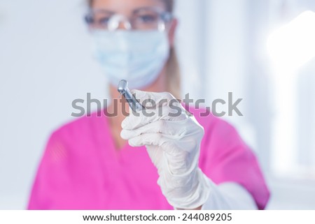 Dentist in surgical mask and scrubs holding tool at the dental clinic
