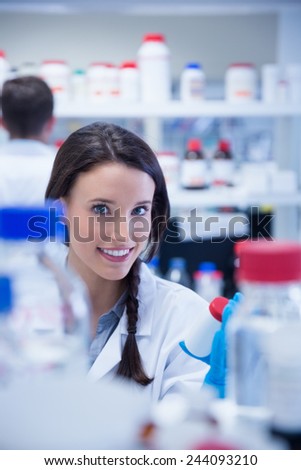 Smiling chemist picking up the bottles on the shelf in lab