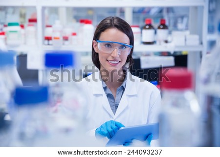 Smiling chemist wearing safety glasses and using tablet pc in lab