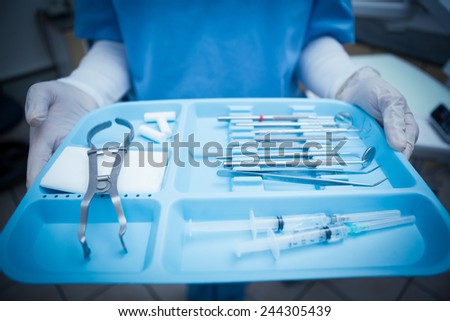 Close up mid section of female dentist in blue scrubs holding tray of tools