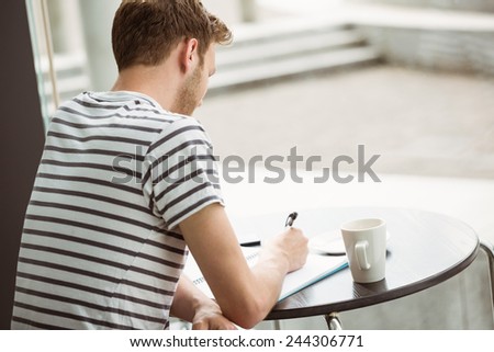 Student sitting with a hot drink and writing on notepad in cafe at the university