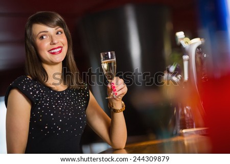 Pretty brunette drinking glass of champagne in a bar