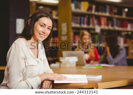 Smiling student sitting at desk reading text book in library