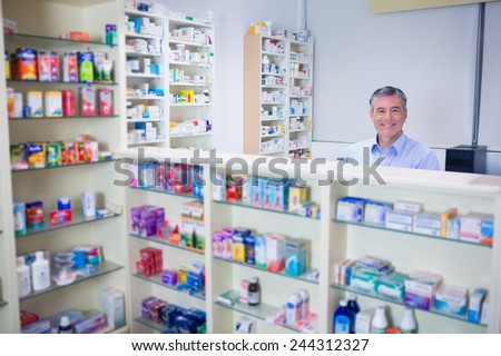 Pharmacist with grey hair standing behind shelves of drugs in the pharmacy