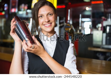 Happy barmaid smiling at camera making cocktail in a bar
