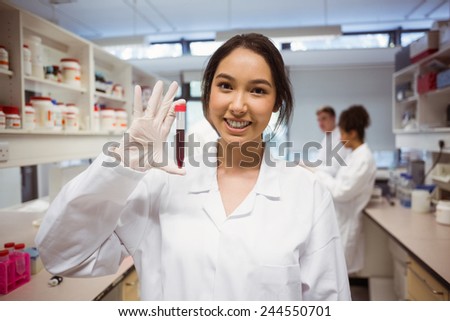 Pretty science student smiling and showing vial at the university