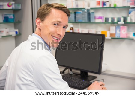Happy pharmacist using the computer at the hospital pharmacy