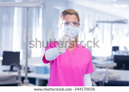 Dentist in surgical mask and scrubs holding syring at the dental clinic