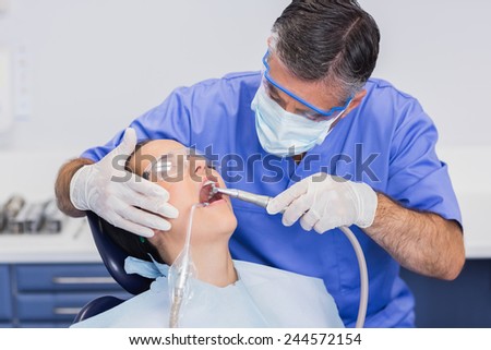 Dentist wearing surgical mask and safety glasses examining a patient