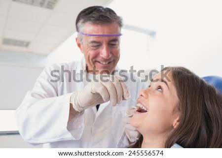 Pediatric dentist using dental floss to his young patient in dental clinic